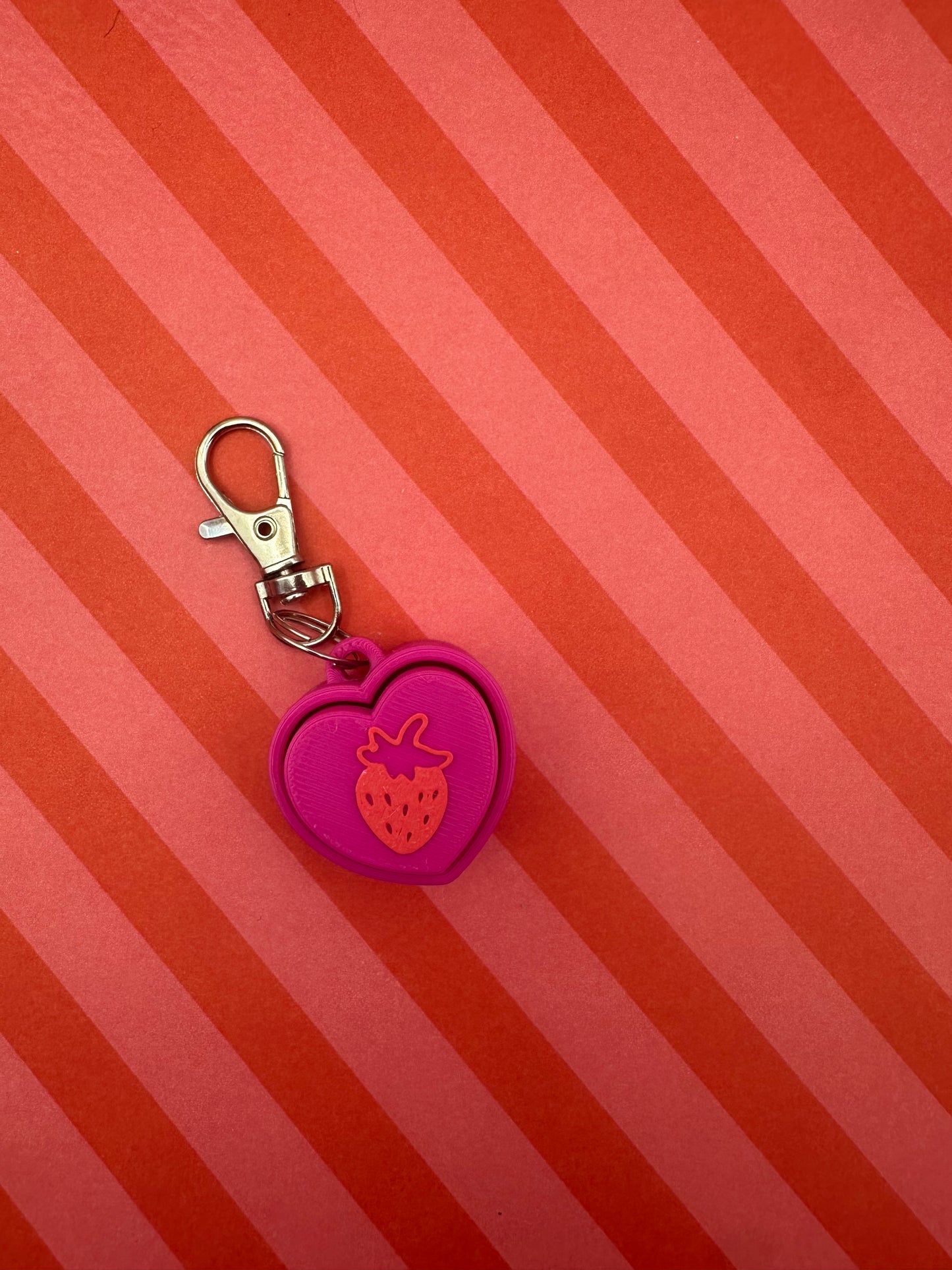Pink keychain with strawberry design on a red and orange striped background