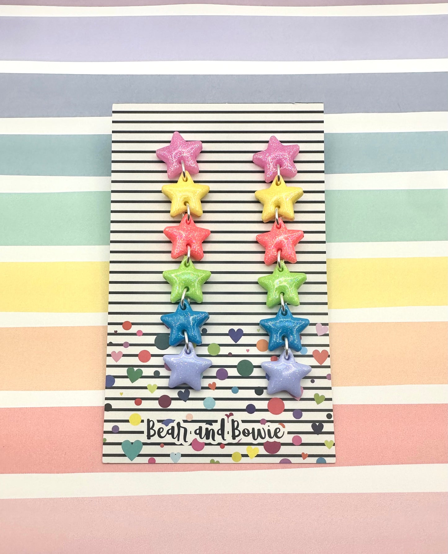 Colorful star-shaped earrings on a striped background with 'Bear and Bowie' branding.