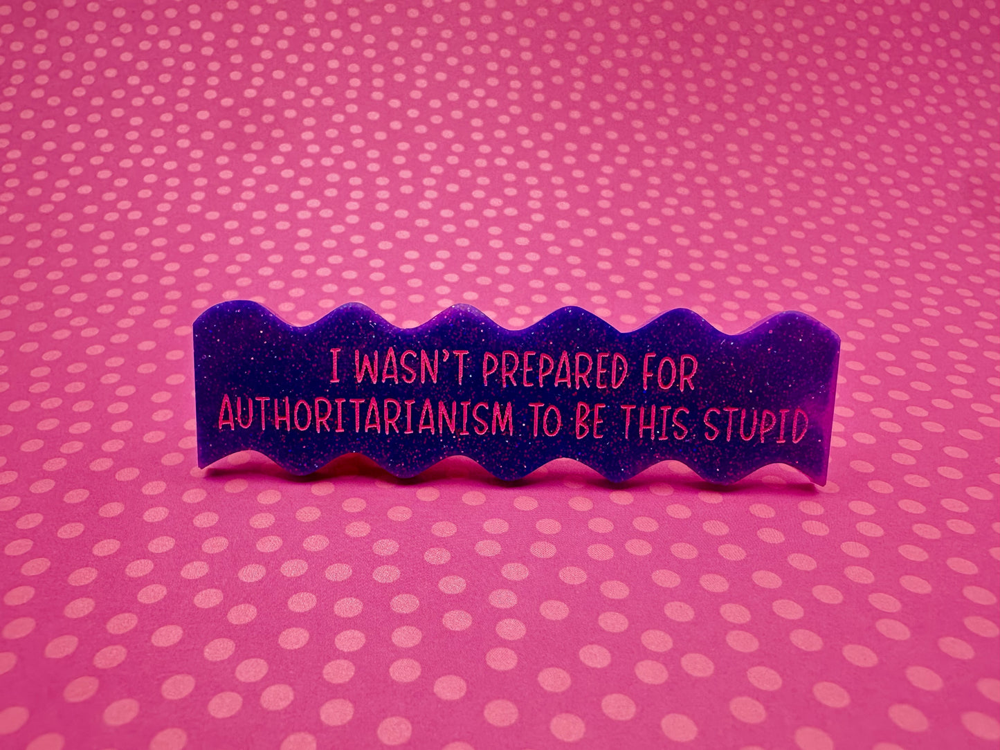 Purple wavy hairclip with text "I wasn't prepared for authoritarianism to be this stupid" on a pink polka dot background