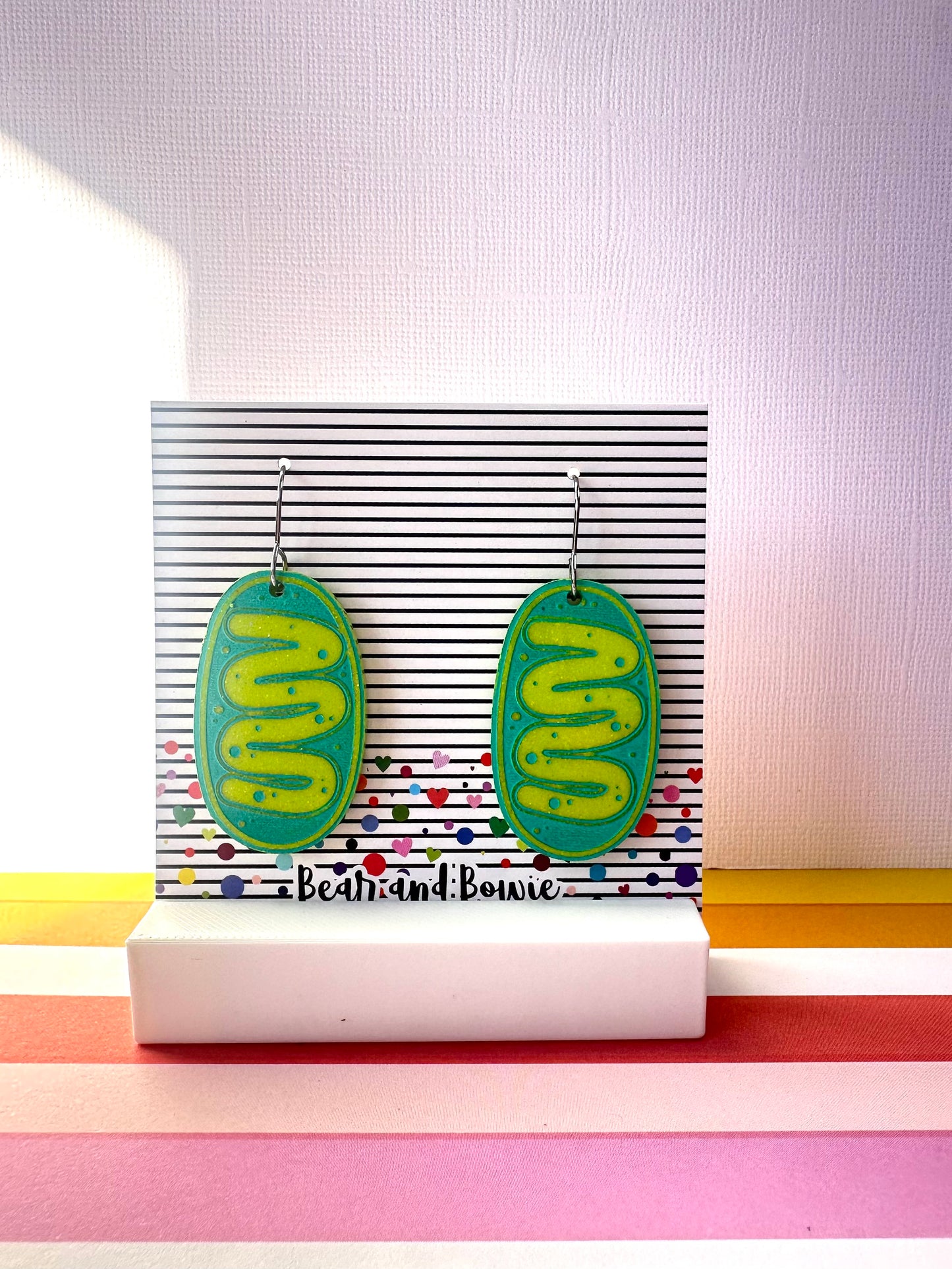 Pair of green and teal mitochondria earrings on a stand with colorful background