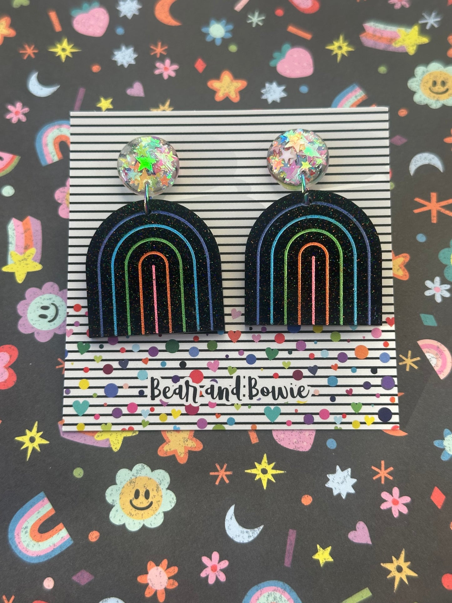 Colorful rainbow earrings on a patterned background