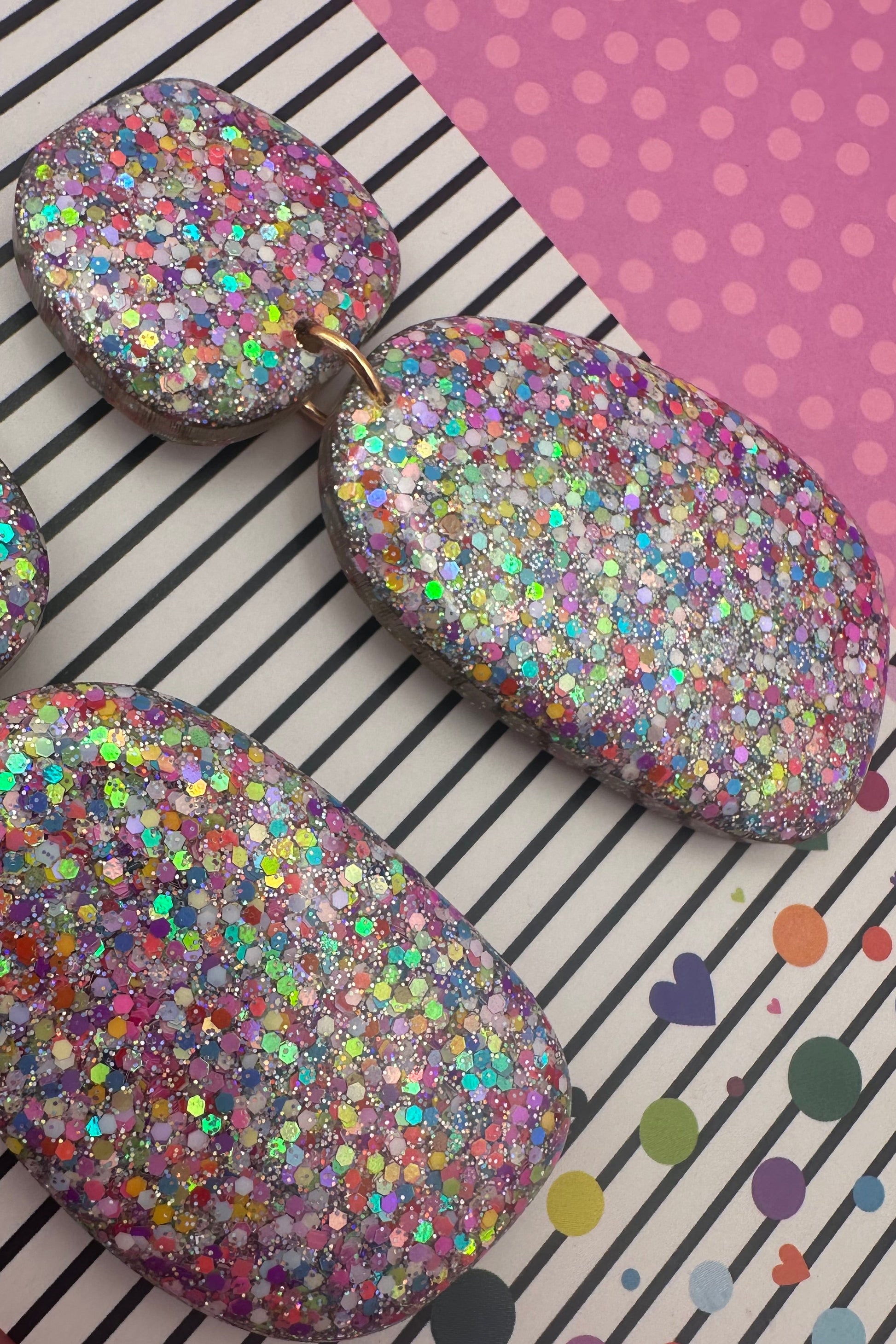 Multicolored glittery earrings on a striped and polka dot background