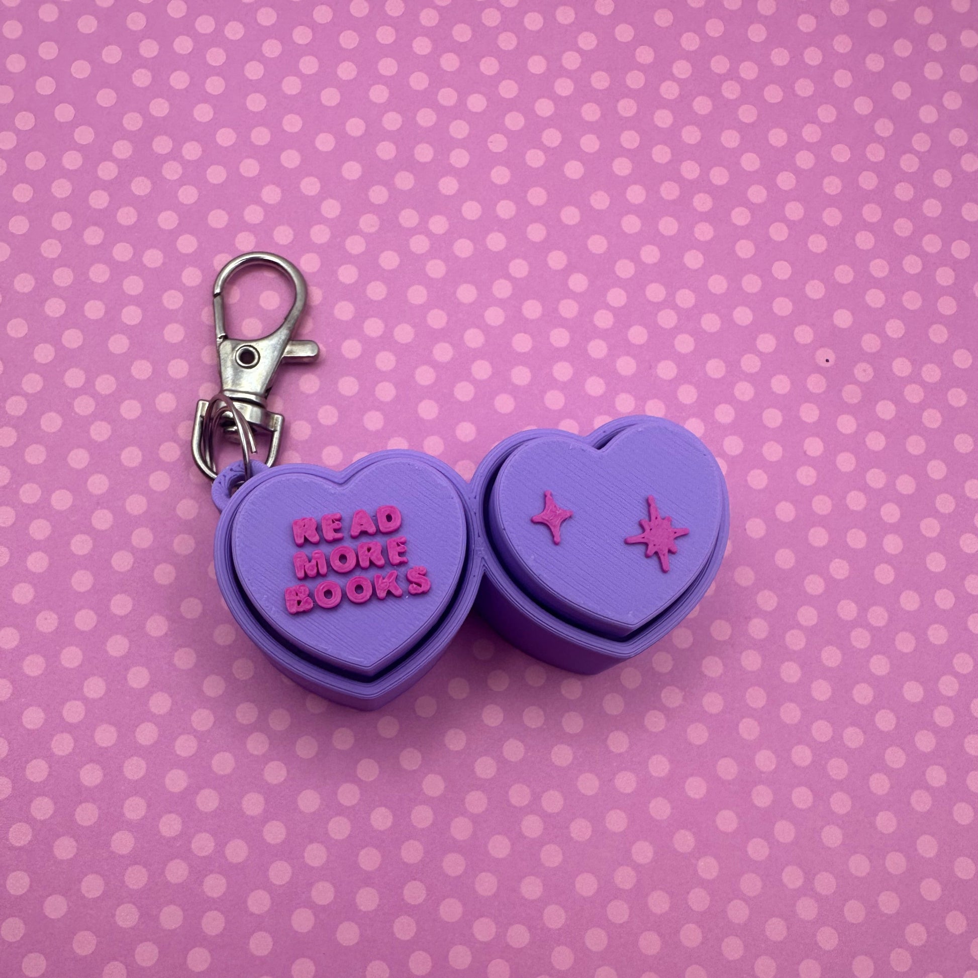Purple heart-shaped keychain with 'Read More Books' text on a pink polka dot background