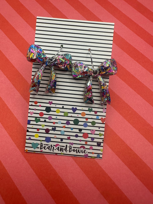 Colorful bow earrings on a striped card with 'Bear and Bowie' branding against a red and pink striped background.