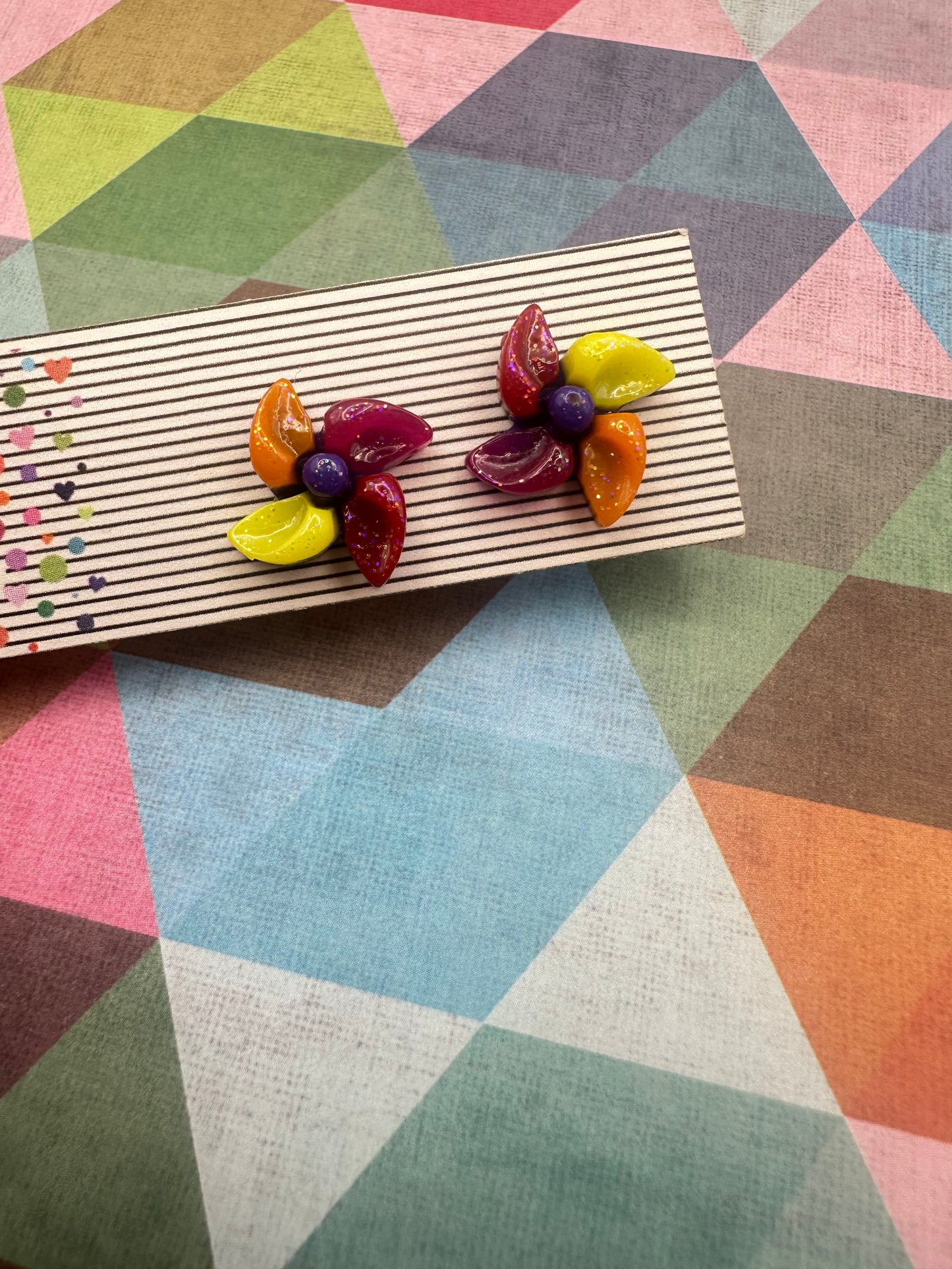 Colorful pinwheel stud earrings on an earring card against a geometric patterned background