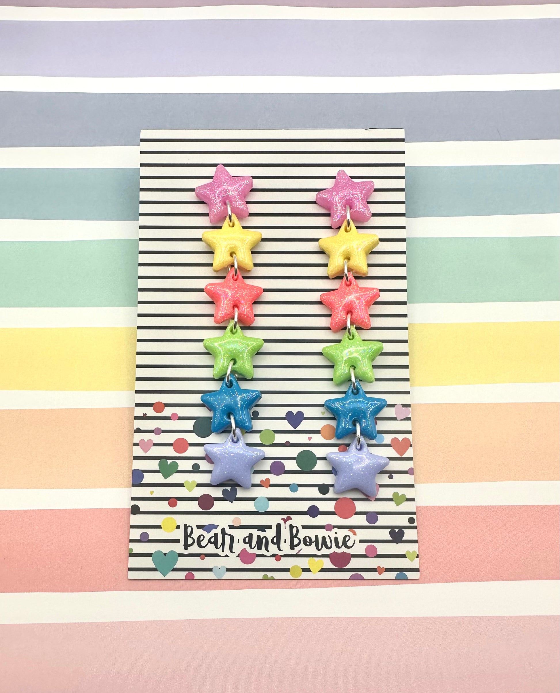 Colorful star-shaped earrings on a striped background with 'Bear and Bowie' branding.