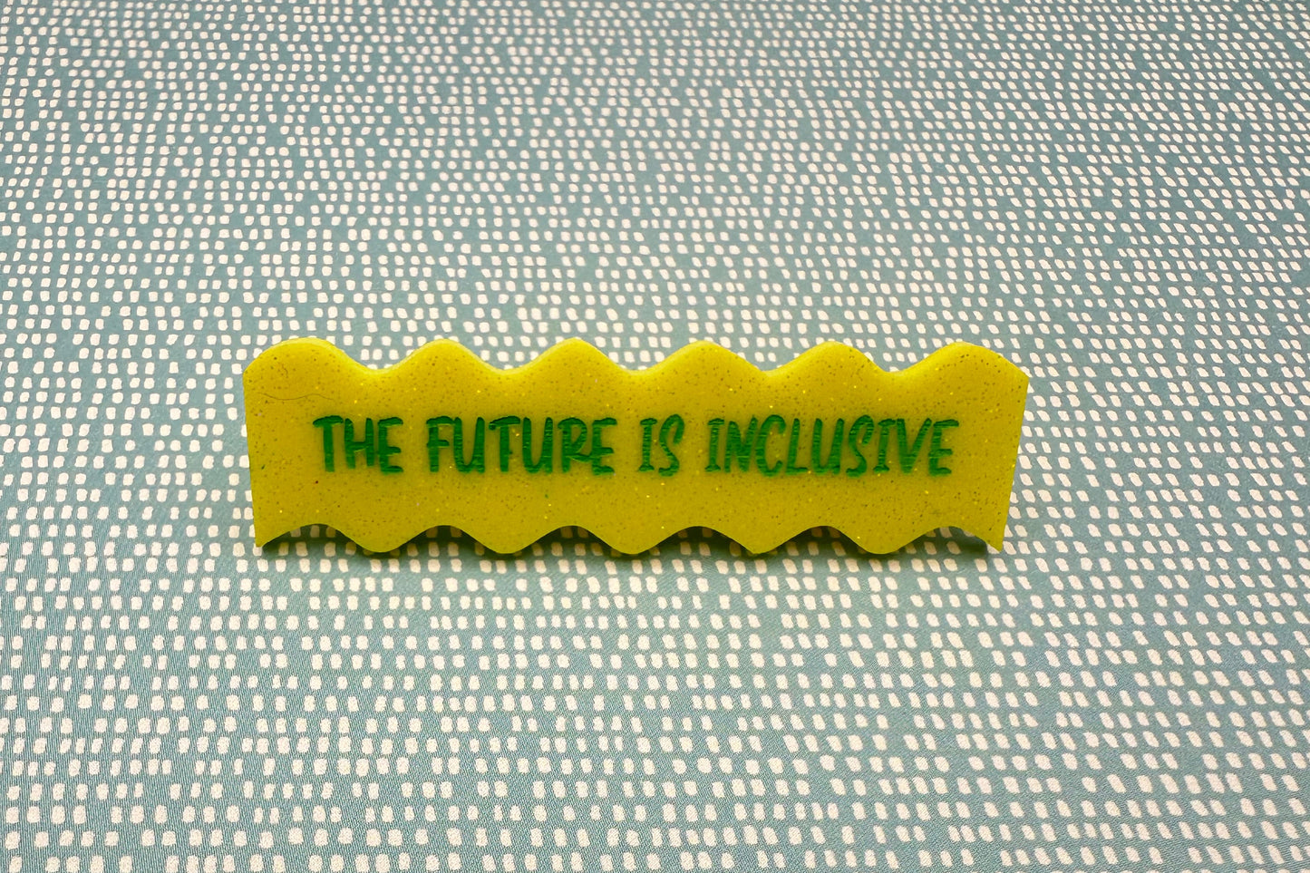 Yellow hairclip with 'The Future is Inclusive' text on a textured fabric background