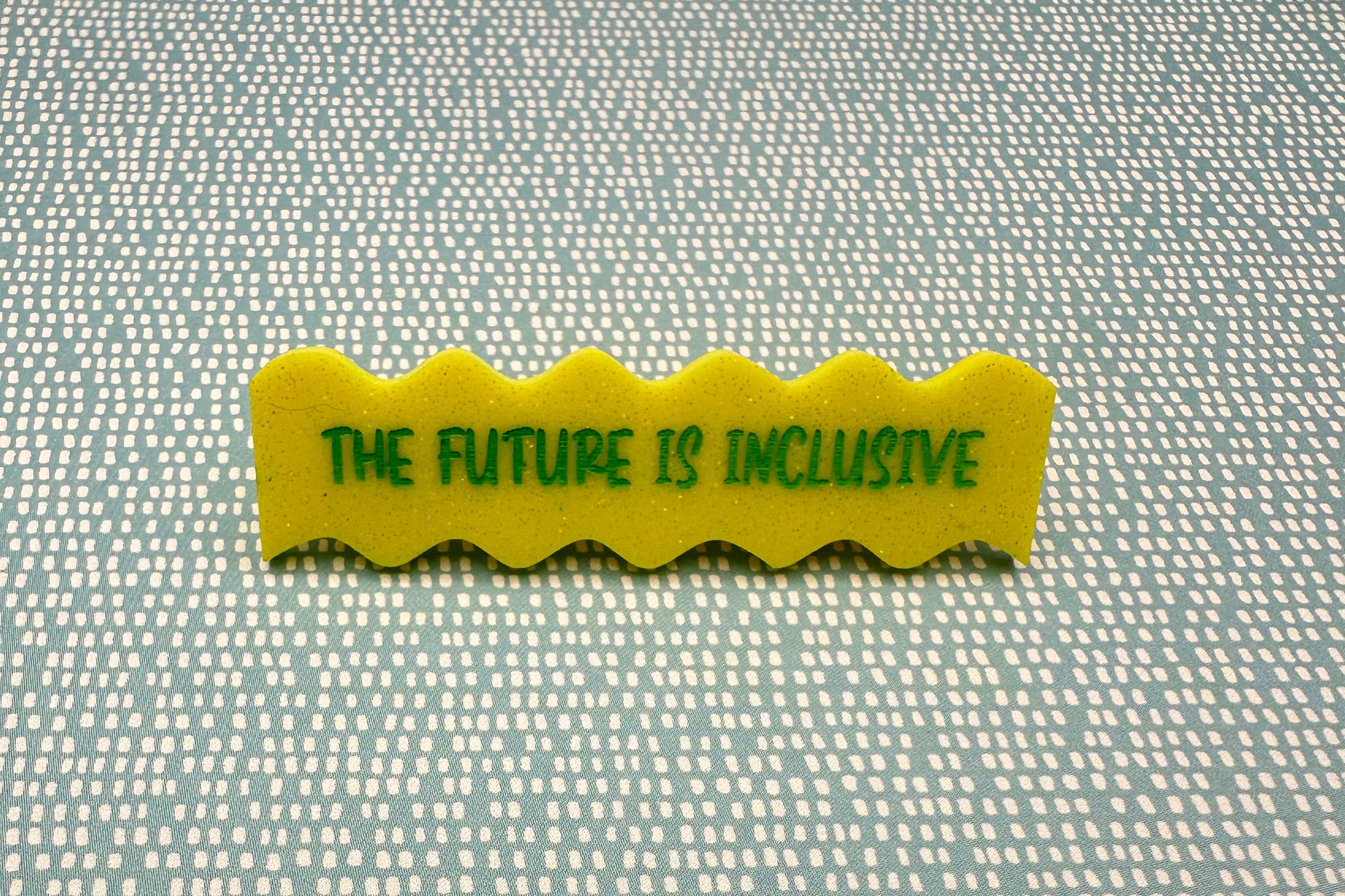 Yellow hairclip with 'The Future is Inclusive' text on a textured fabric background