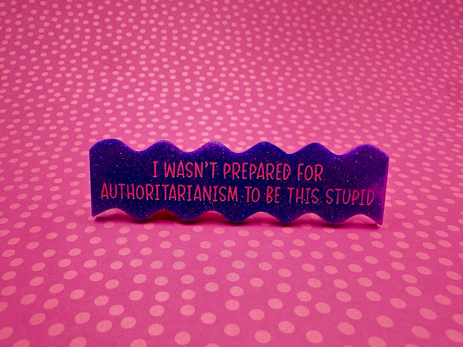 Purple wavy hairclip with text "I wasn't prepared for authoritarianism to be this stupid" on a pink polka dot background
