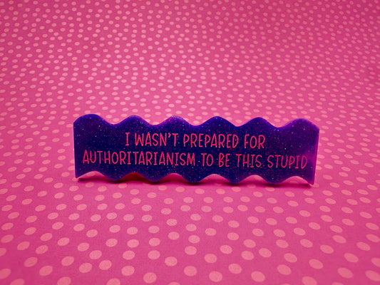 Purple wavy hairclip with text "I wasn't prepared for authoritarianism to be this stupid" on a pink polka dot background