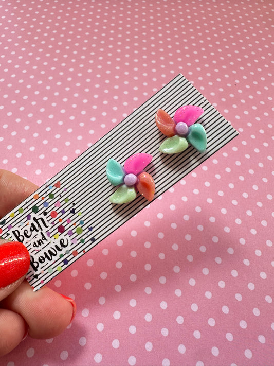 Colorful and bright pinwheel earrings on an earring card against a pink dotted background