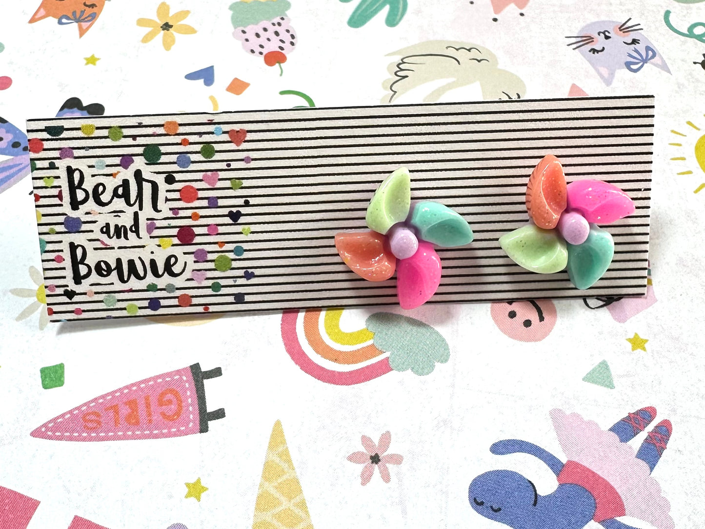 Colorful pinwheel stud earrings on a striped card with 'Becky and Bowie' branding against a playful background.