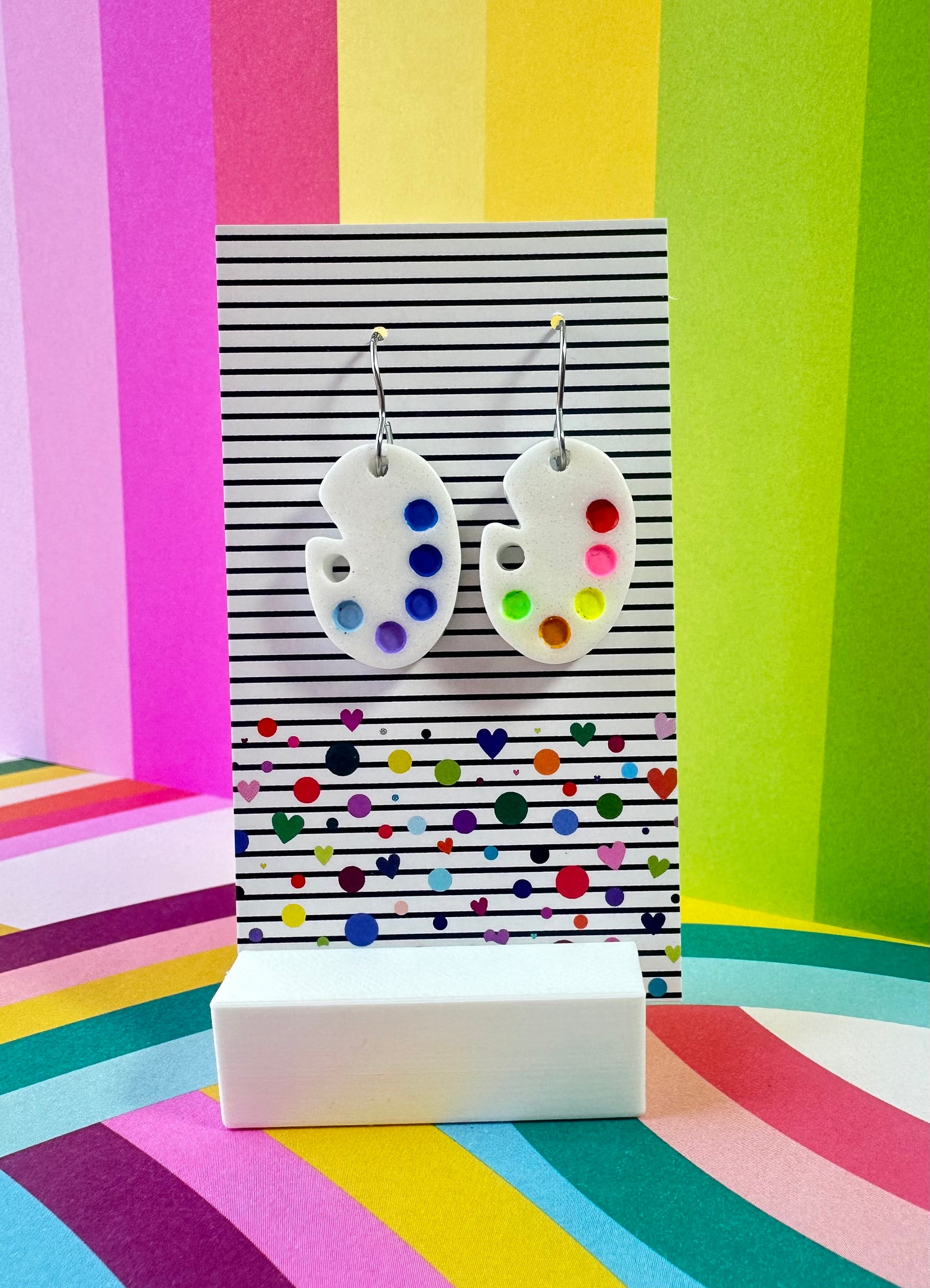 Pair of artist palette earrings on a colorful striped background