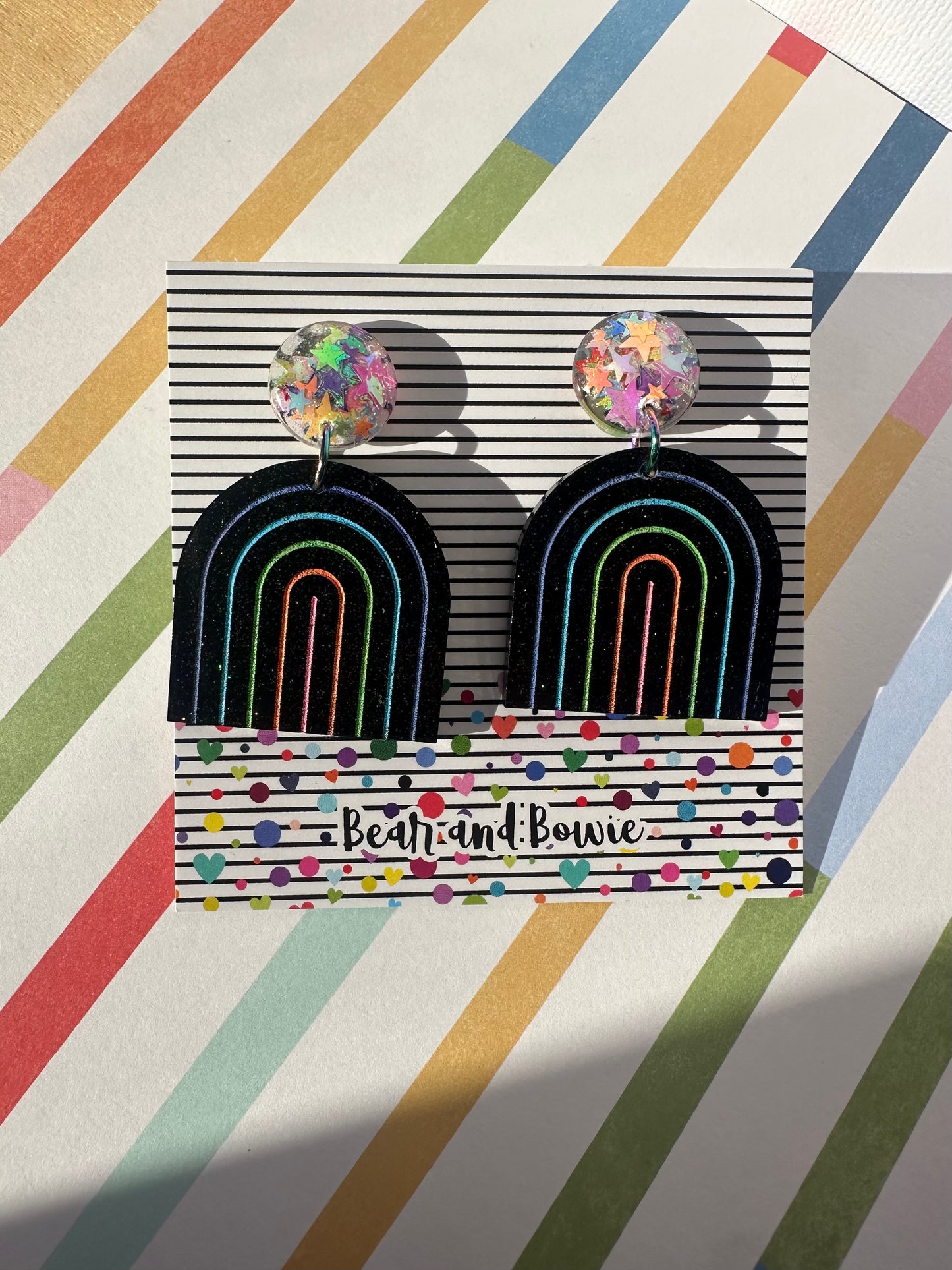 Pair of rainbow earrings in a 'Bear and Bowie' packaging on a striped background