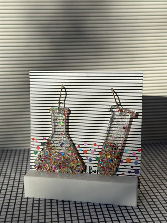 Glitter test tube and erlenmyer flask earrings with colorful glitter on a striped background