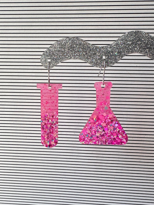 Pink glitter test tube and erlenmeyer flask earrings on a striped background