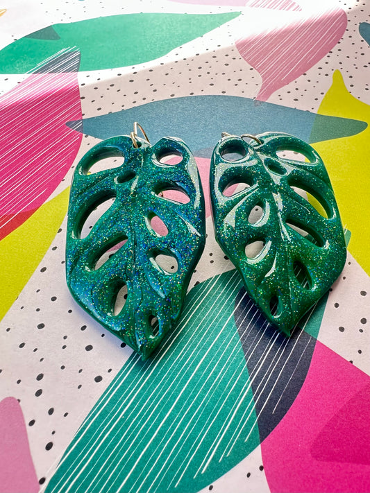 Green leaf-shaped earrings on a colorful abstract background